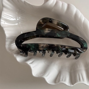 Detailed top view of large marble texture acetate hair claw clip in a white shell tray