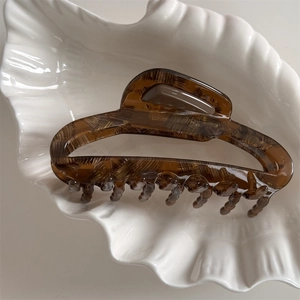 Macro shot of amber tortoiseshell hair claw with refined texture in a white shell dish
