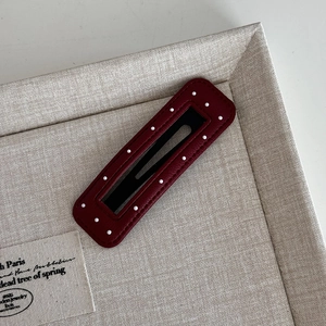 Detail of burgundy rectangular hair clip with white polka dots on soft fabric tray