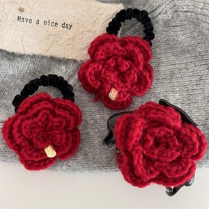 Dettaglio molletta a rosa all'uncinetto rossa e elastici su sfondo a maglia morbida