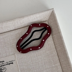 Macro detail of dark red polka dot leather wave hair clip on a beige textured tray