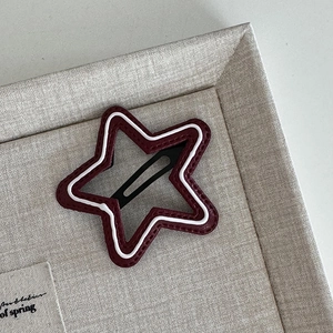 Macro detail of wine red star-shaped leather hair clip with white stitching on a tray