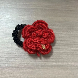 Dettaglio del fermaglio per capelli a fiore rosso all'uncinetto con tag dorata