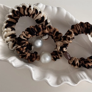 Set de trois chouchous motif léopard avec perles blanches et dentelle sur plateau coquille