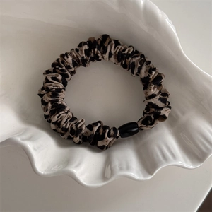 Détail d'un chouchou léopard avec texture plissée et perle noire sur un plateau blanc