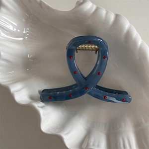 Detailed close-up of matte blue hair claw with red polka dots on white shell decor