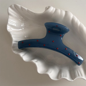 Detail view of a navy blue hair claw with red polka dots placed in a shell plate