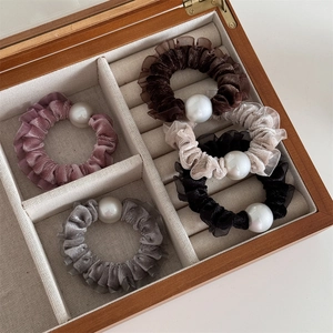 Detail of five velvet pearl scrunchies in varied colors within a wooden jewelry box