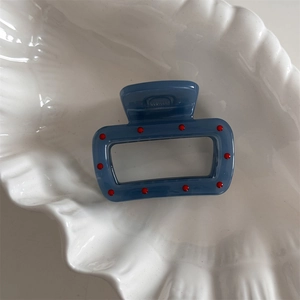 Detail of rectangular blue hair claw with red polka dots in a white shell dish