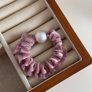 Detailed close-up of a purple velvet scrunchie with a large glossy white pearl on it