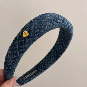 Detail of navy blue plaid headband with a golden heart-shaped metal logo and handmade label