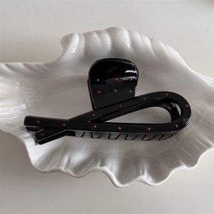 Polished black hair claw clip with red polka dots on a white shell ceramic tray