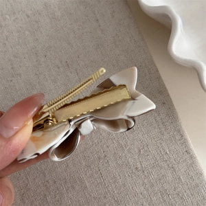 Detail of a marble-textured acetate bow hair clip with a sturdy gold metal fastener