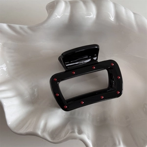 Close-up of a glossy black hair claw clip with red polka dots in a white shell dish