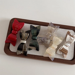 Set of six colorful handmade acetate bow hair clips in various patterns on a wooden tray