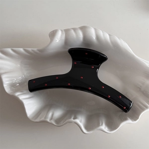 Close-up of a glossy black hair claw clip featuring red polka dots on a shell plate
