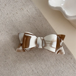 Close-up of a double-layered bow hair clip in marble acetic acid with golden engraving