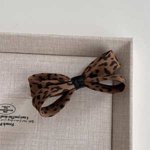 Dettaglio di fermaglio per capelli con fiocco leopardato e nastro nero in scatola di lino