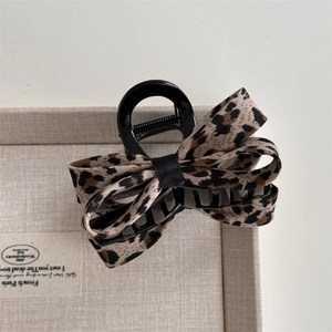 Dettaglio del fermaglio per capelli con fiocco leopardato su sfondo di tessuto beige