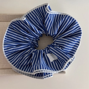 Detail of blue striped scrunchie with white stitching and silver bow fabric label