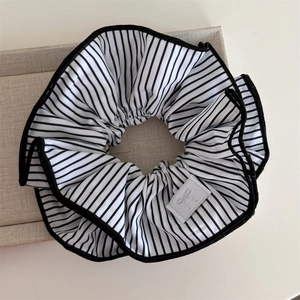 Close-up of a striped scrunchie with a silver bow tag and black piping edges