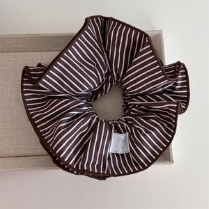 Detail of a large striped scrunchie in brown and white on a linen tray with soft lighting