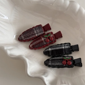 Detail of sweet plaid hair clips with cherry decor on a white ceramic tray