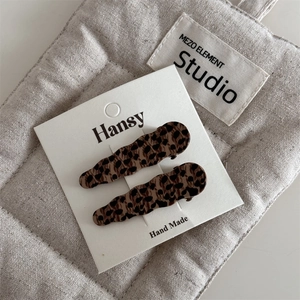 Detail of two leopard print hair clips with wavy edges on a grey quilted fabric bag