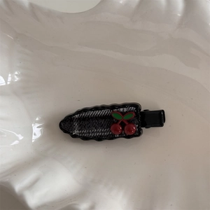 Detail of checkered hair clip with red cherry charm in a white shell-shaped dish