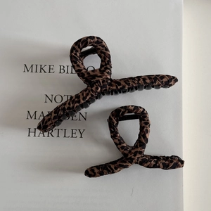 Detail view of large and small leopard print fabric wrapped claw clips on minimalist background