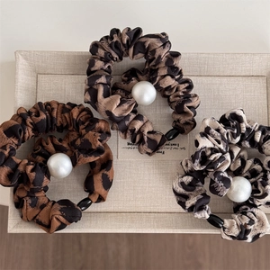 Three leopard print scrunchies with white pearl details in warm brown and gray tones