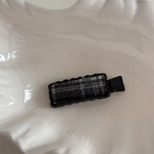 Detail of the sweet black wavy hair clip with gray checkered fabric on a white plate