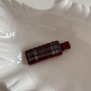 Detail of vintage red plaid hair clip with wavy resin edges on a ceramic shell tray