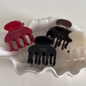 Detail view of four glossy hair claws in wine, black, brown, and cream on a white tray