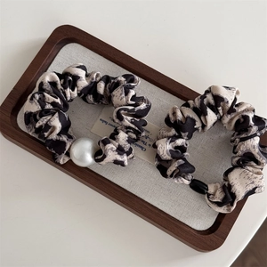 Detail view of leopard print hair scrunchies with elegant pearl accents on a wooden tray