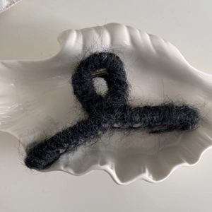 Primer plano de pinza de pelo de felpa negra con textura suave de piel sintética en plato