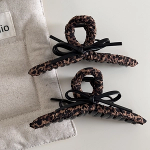 Close-up of leopard print hair claws with black leather bows on a neutral background
