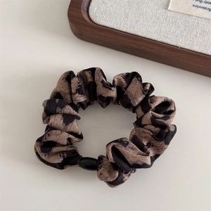 Detail of leopard print scrunchie with soft fabric texture and black pearl buckle detail
