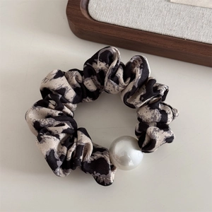Detail of marble pattern fabric scrunchie with large pearl accent on a minimalist setup