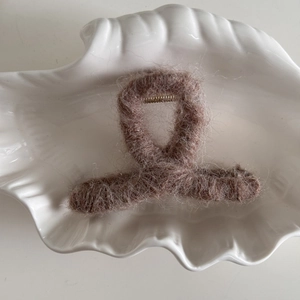 Detalle de pinza para el pelo de felpa caqui sobre una bandeja en forma de concha