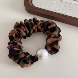 Close-up of leopard print scrunchie with a large pearl accent on a beige surface