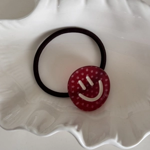Detail of red polka dot charm with smiley face on a black elastic hair tie
