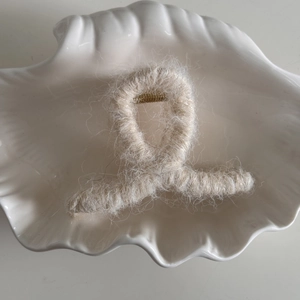 Detalle de pinza de pelo de felpa blanca crema con resorte metálico dorado en un plato