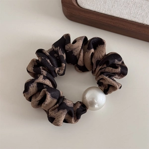 Detailed view of leopard print hair scrunchie with large pearl accent on beige surface