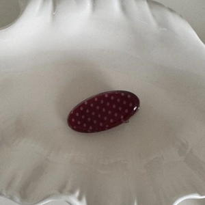 Close-up of retro burgundy hair clip with cream polka dots on a white tray