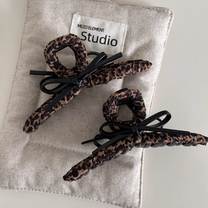 Leopard print hair claw clips with black leather bows on elegant linen background