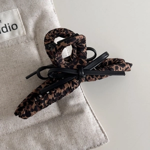 Detail of leopard print hair claw clip featuring a black leather bow and textured finish