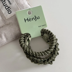 Detail view of olive green elastic hair ties with woven texture on branded packaging