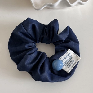 Detailed view of navy denim scrunchie with blue bead and white vintage label on white tray