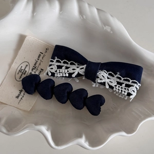 Dark blue bow hair clip with white lace and heart-shaped fabric clips on ceramic tray